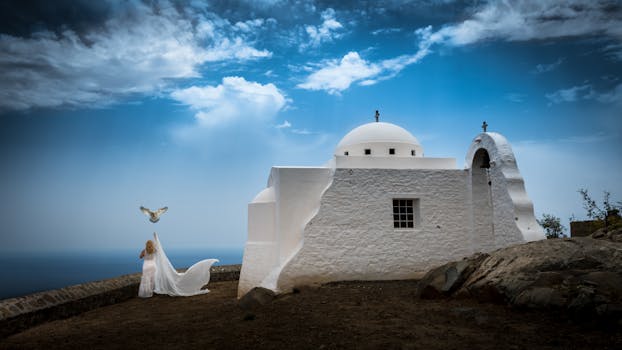 在悬崖边一座白色教堂旁，蓝天下，一个女人和一只鸽子构成了一幅宁静的场景
