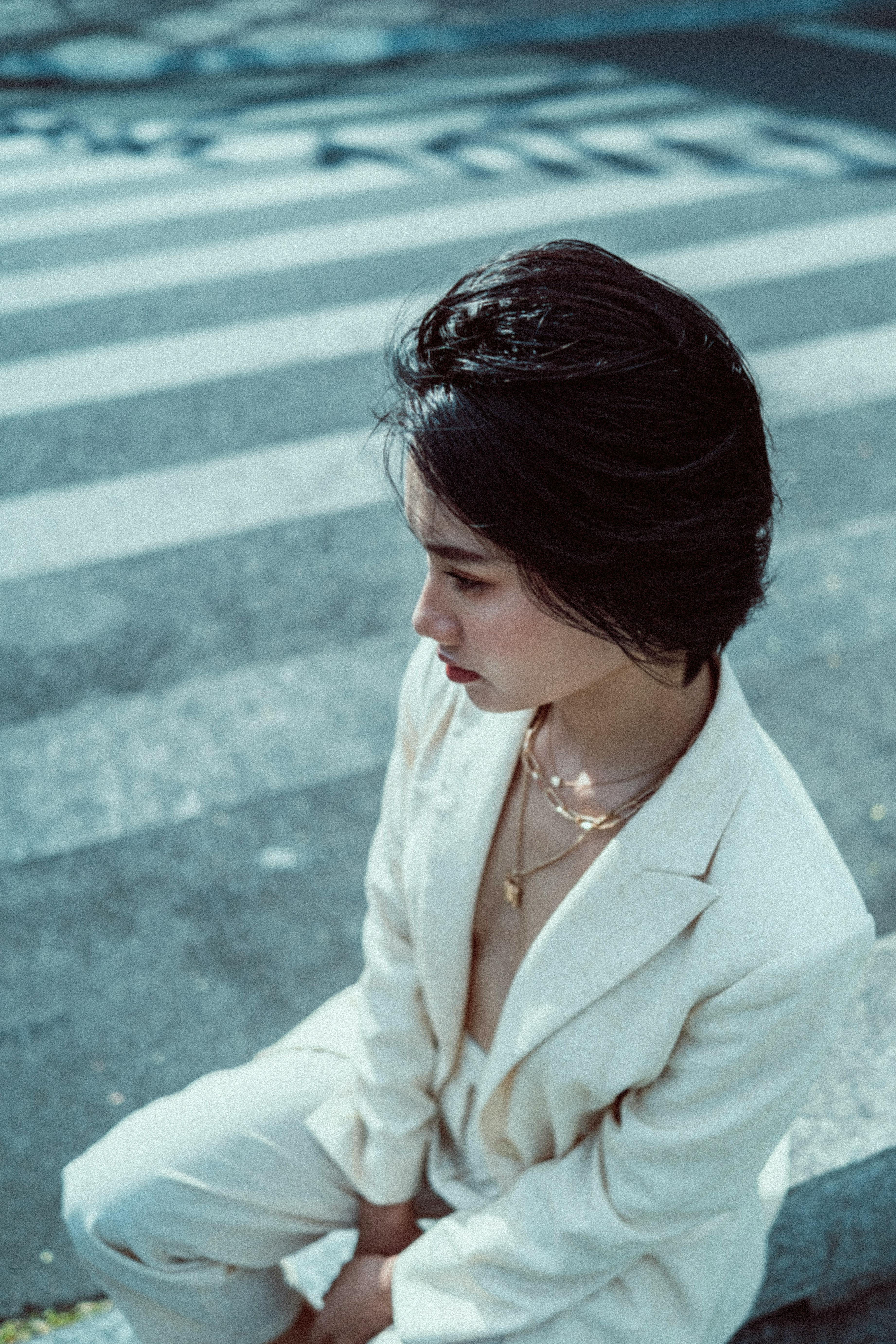 Side profile of a woman in a white suit sitting on a city street. Calm urban portrait.