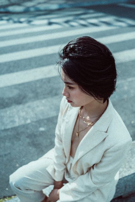 Side profile of a woman in a white suit sitting on a city street. Calm urban portrait.