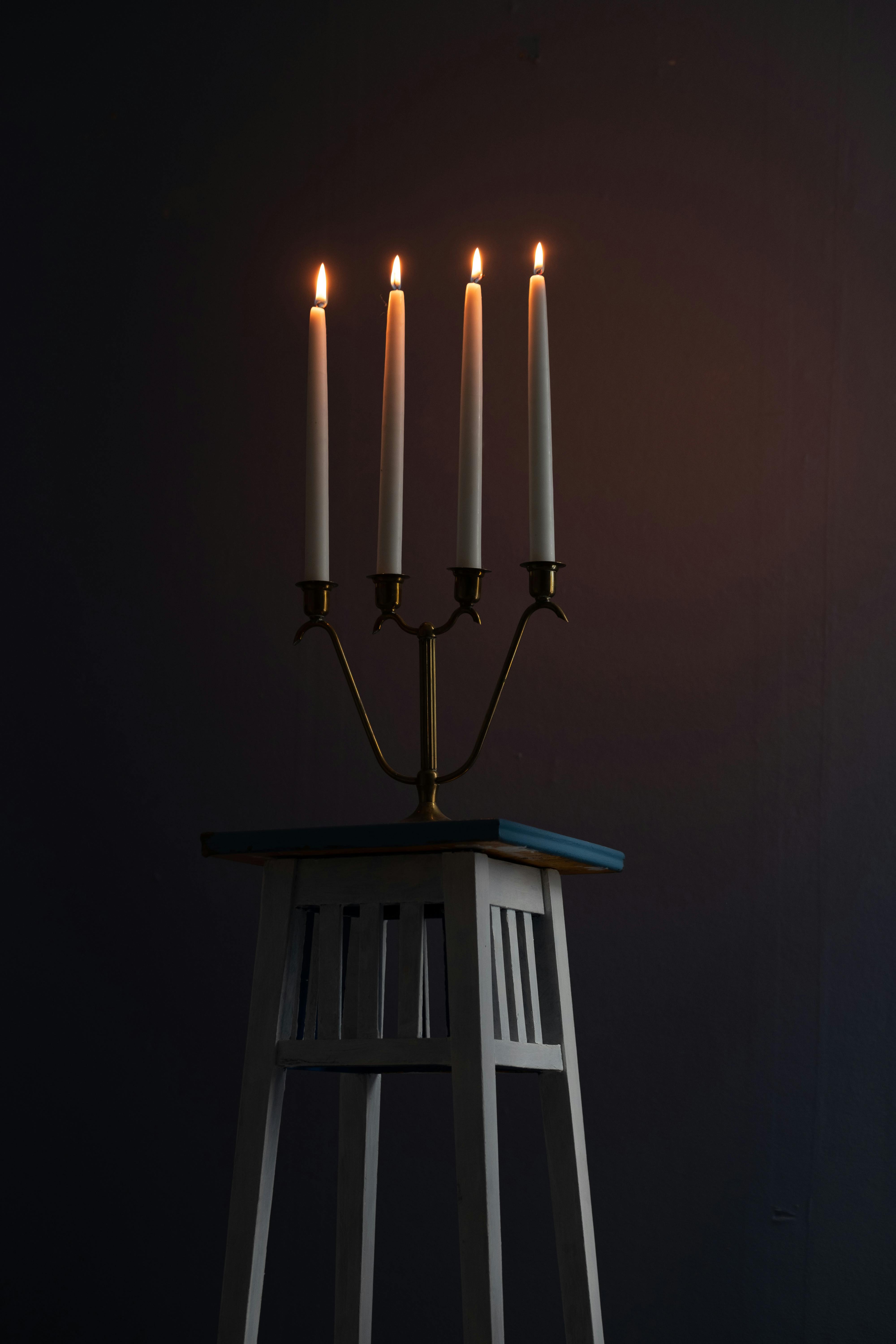 A brass candelabra with lit candles atop a wooden stand in a dark, moody setting.