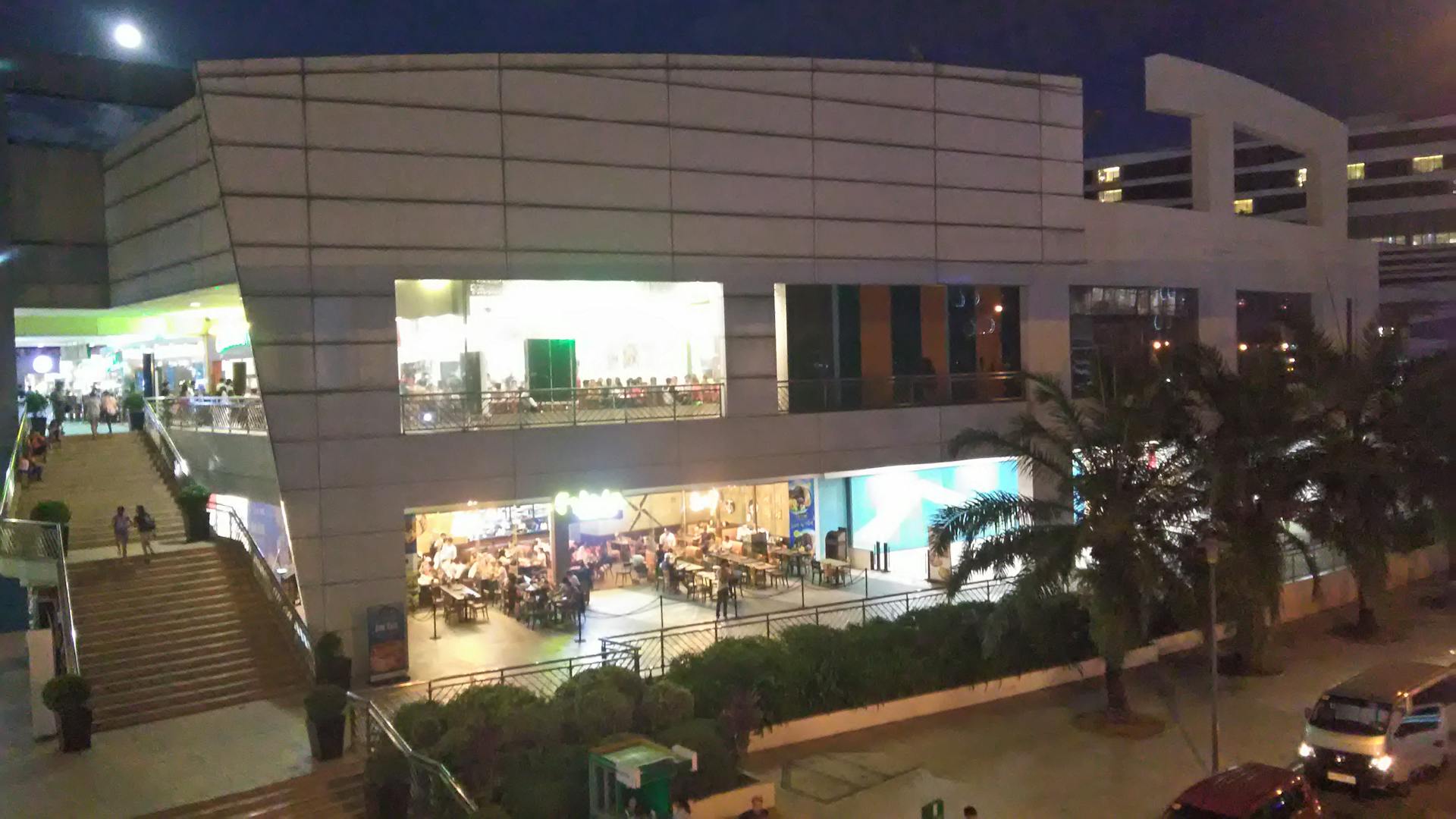 A bustling shopping mall in Pasay City, Philippines, illuminated at night with people and vehicles in view.