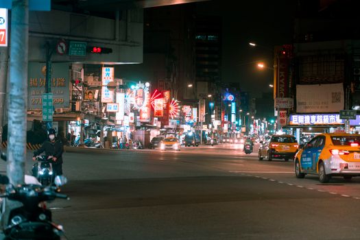 Bustling nighttime city street with glowing neon signs and moving traffic.