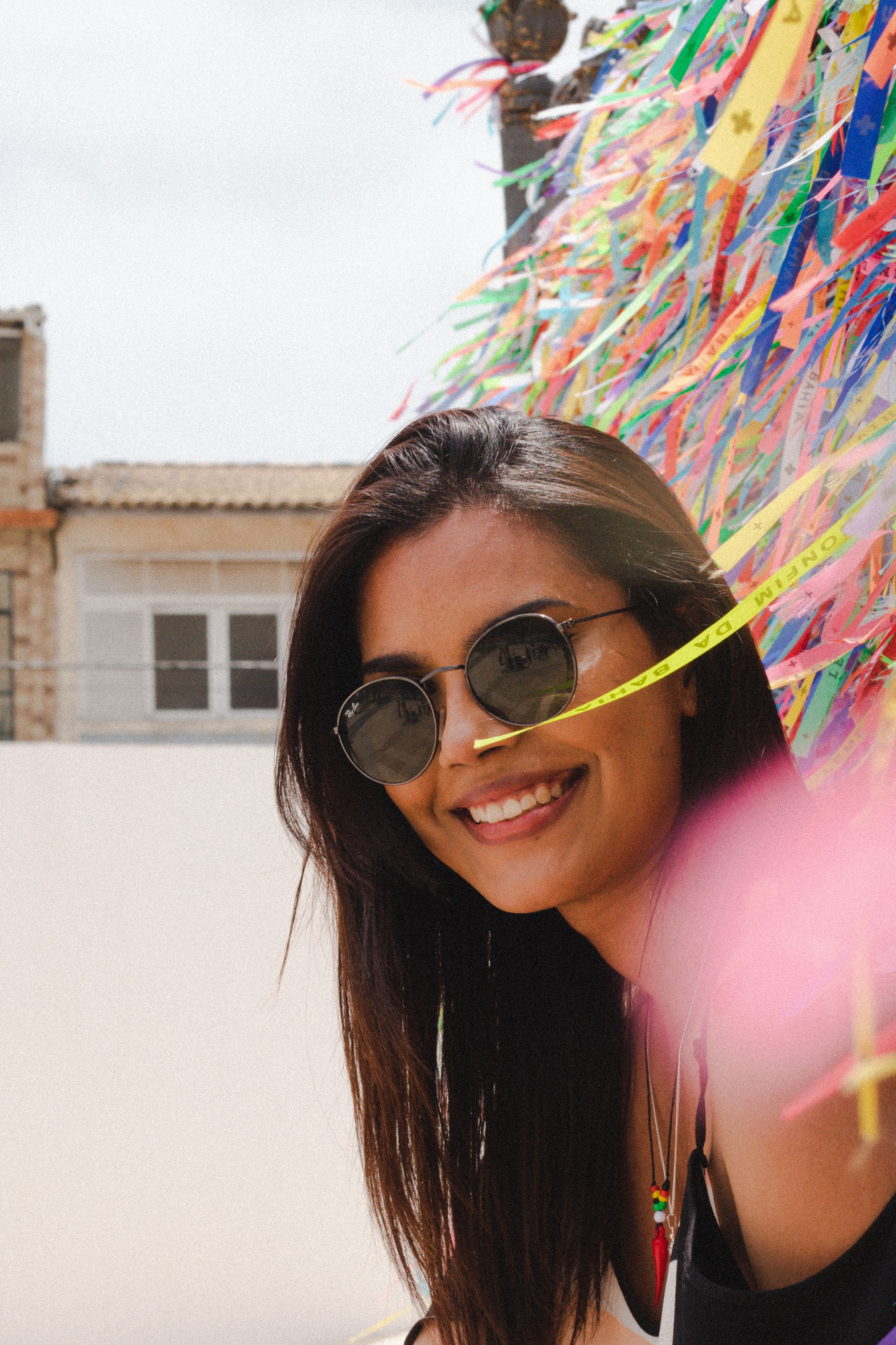 Portrait of a smiling woman in sunglasses, enjoying summer in Salvador, Brazil with colorful ribbons.