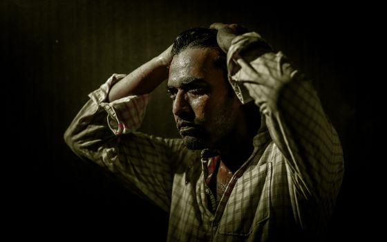 A dramatic portrait of a man in a plaid shirt with a thoughtful, intense expression.