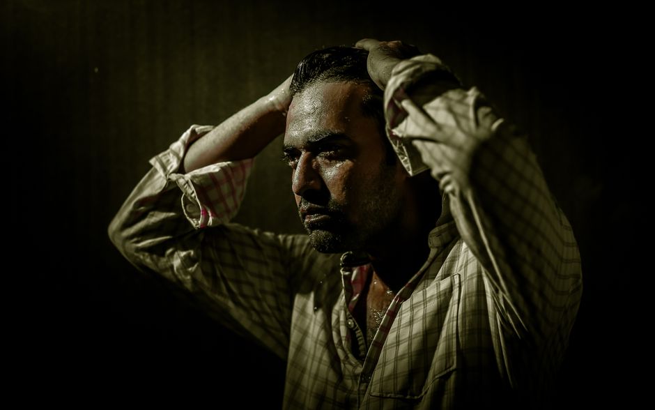 A dramatic portrait of a man in a plaid shirt with a thoughtful, intense expression.