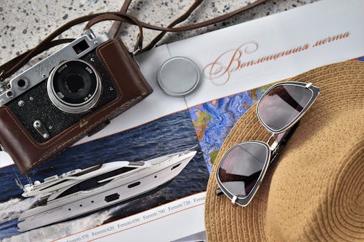 A flat lay of a vintage camera, sunglasses, and travel magazine with a yacht image.
