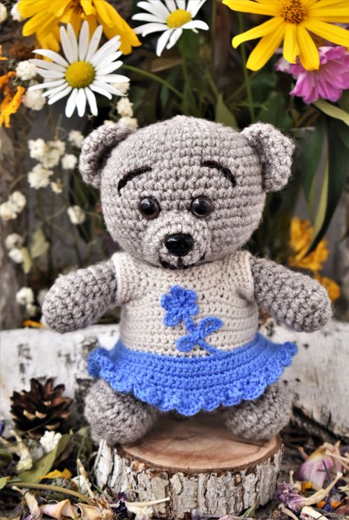 Free Cute crochet teddy bear in a blue outfit surrounded by colorful flowers. Stock Photo