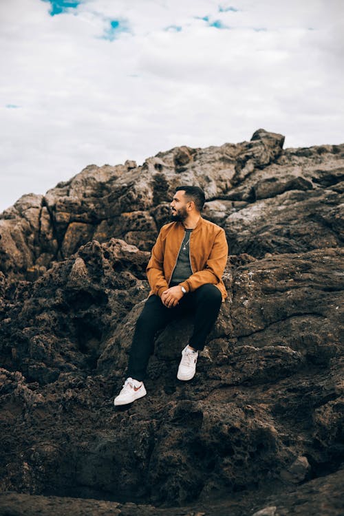 Man in Brown Jacket Sitting on Rock Formation
