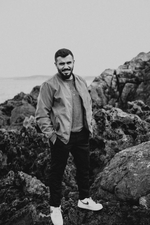 Free Monochrome portrait of a man smiling with hand in pocket on rugged seaside rocks. Stock Photo