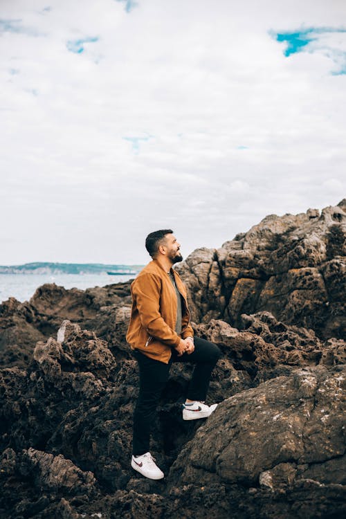 Man in Brown Jacket Standing on Rocky Shore