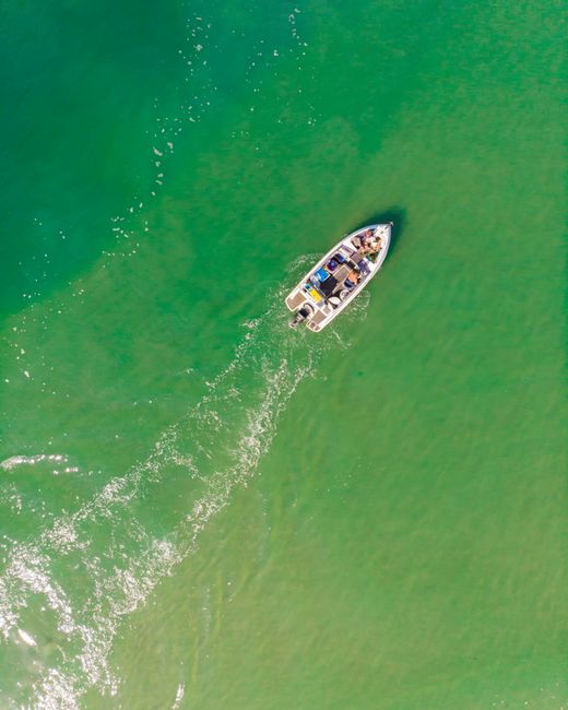 Aerial view of a motorboat navigating through vibrant green open waters, creating ripples.