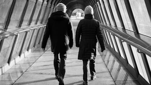 Grayscale Photo of Two People Walking in the Hallway