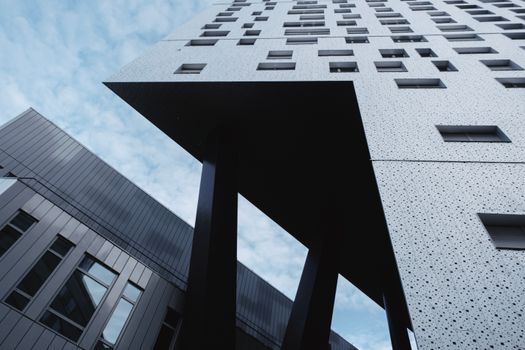 Low-angle view of modern skyscraper with unique geometric design and dotted facade against blue sky.