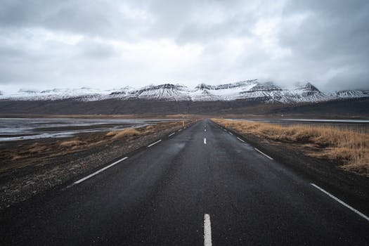 Dramatic road leading to snowy mountains in Iceland under a moody sky.