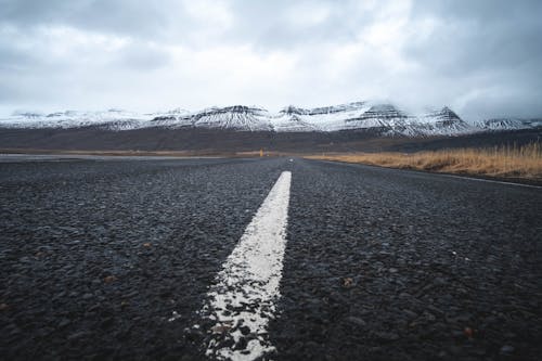 Gray Concrete Road Between Brown Grass Field Under White Clouds