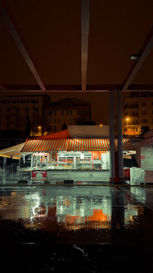 Free A rainy night view of a brightly lit urban street food stall with reflections. Stock Photo