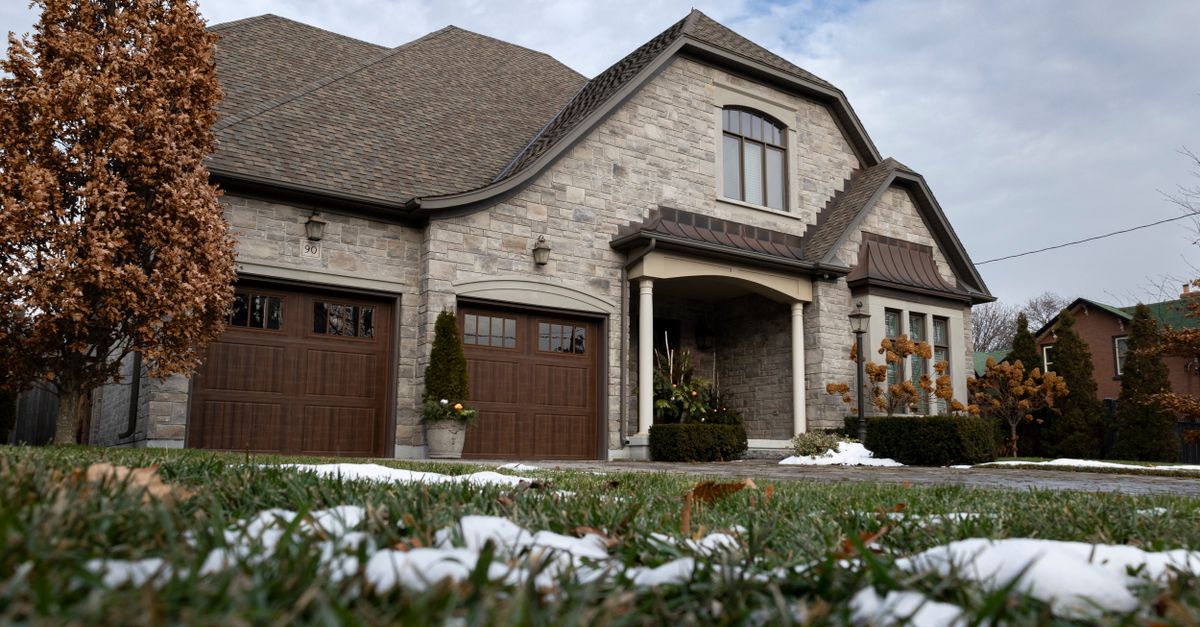 Charming stone house with wooden garage doors and a snow-dusted lawn under a cloudy winter sky.