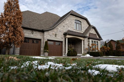 Free Charming stone house with wooden garage doors and a snow-dusted lawn under a cloudy winter sky. Stock Photo