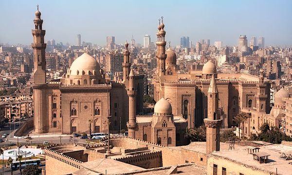 Aerial view of historic mosques with Cairo cityscape backdrop, showcasing Islamic architecture.