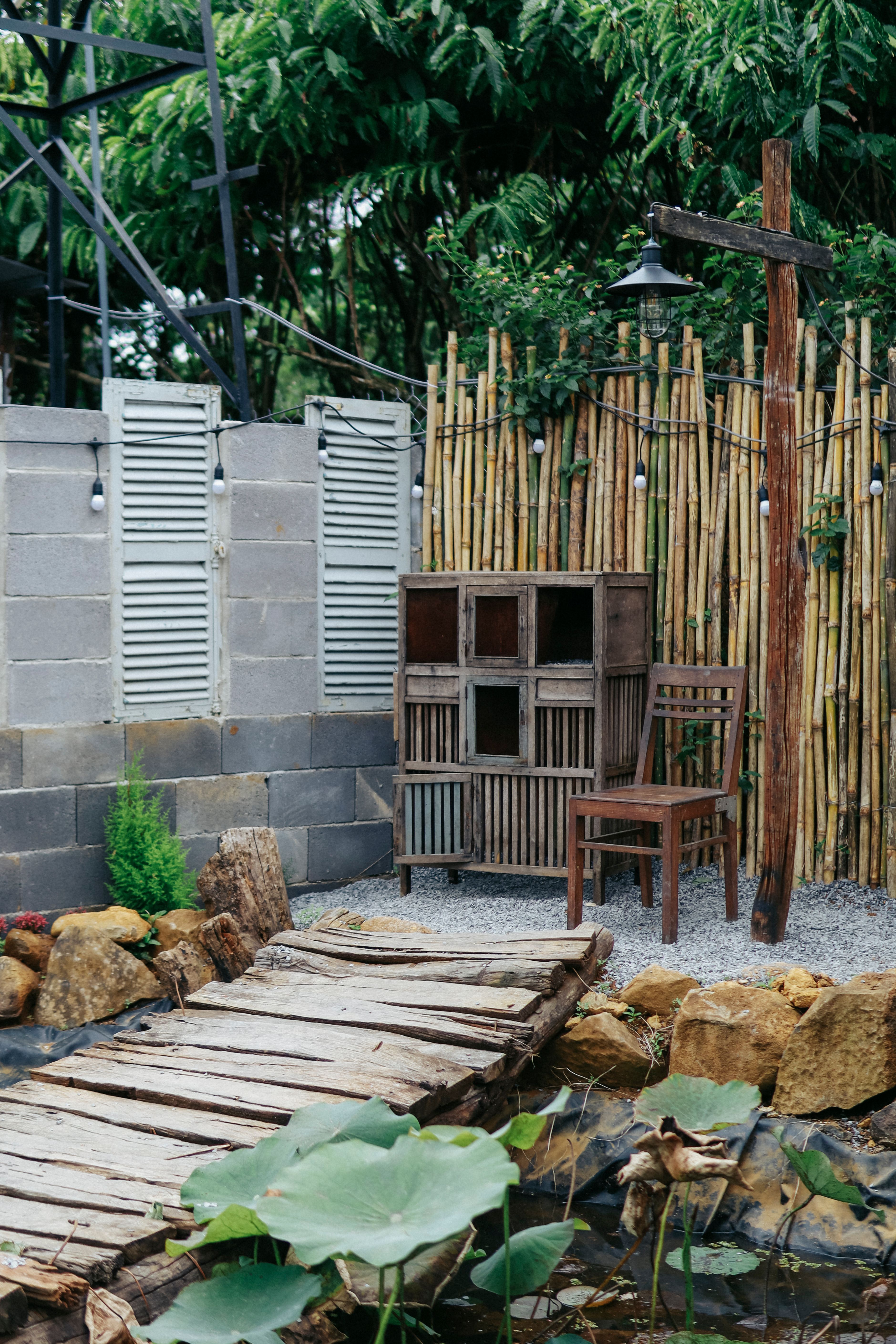 A quaint garden scene featuring a wooden footbridge, bamboo fence, and rustic furniture.