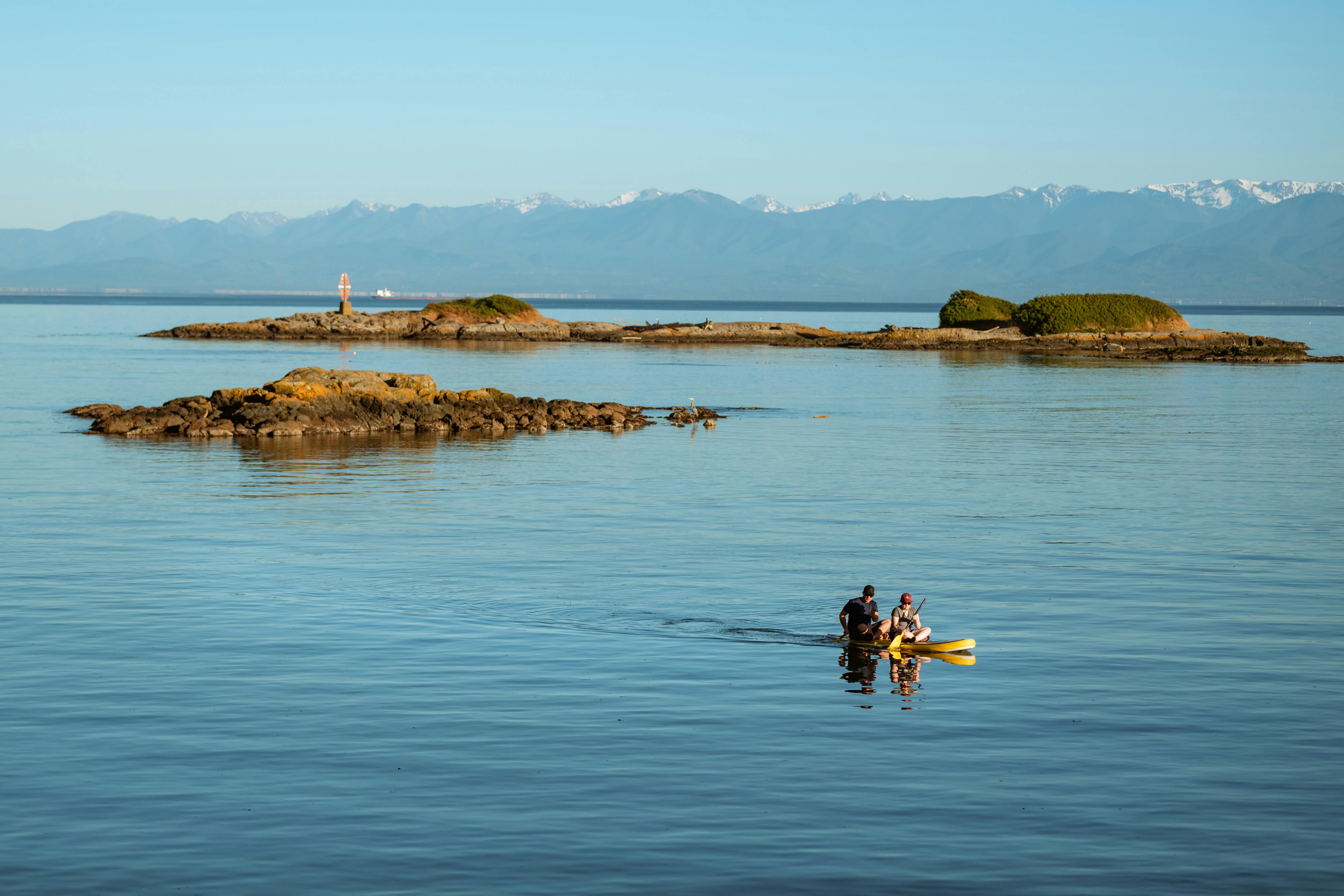 Two people kayaking near rocky islands with mountains in the background, BC, Canada.