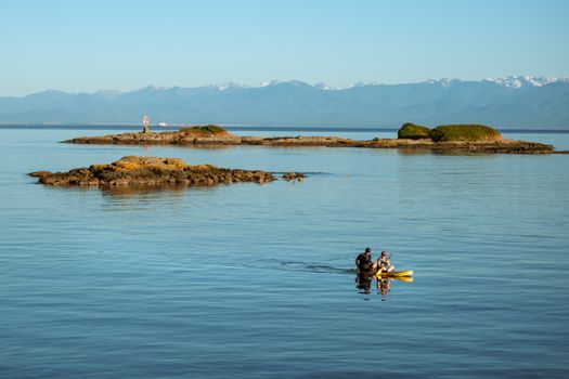 Two people kayaking near rocky islands with mountains in the background, BC, Canada.
