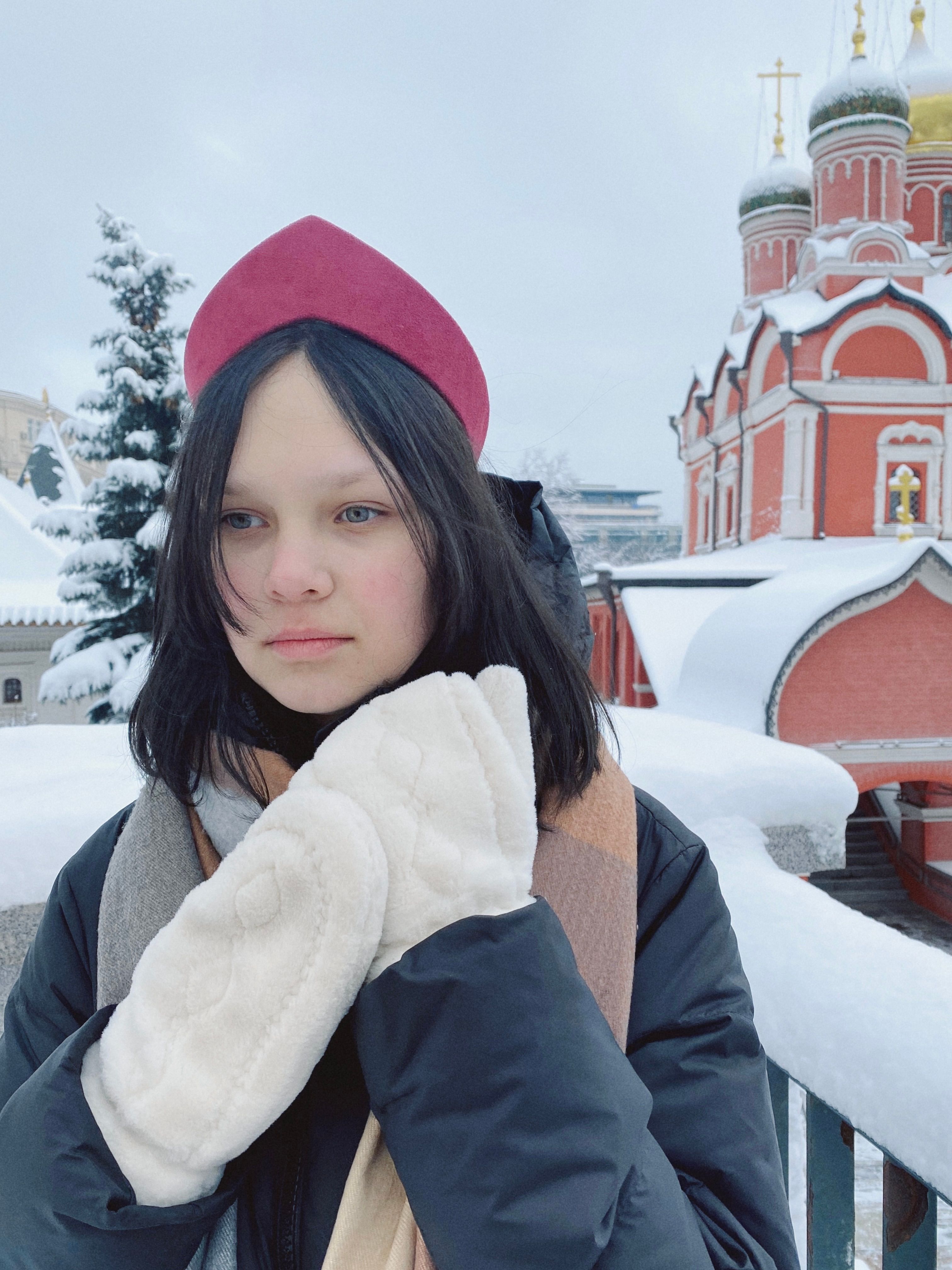 Young woman in winter attire standing in snow with a Russian Orthodox church backdrop. Serene winter scene.