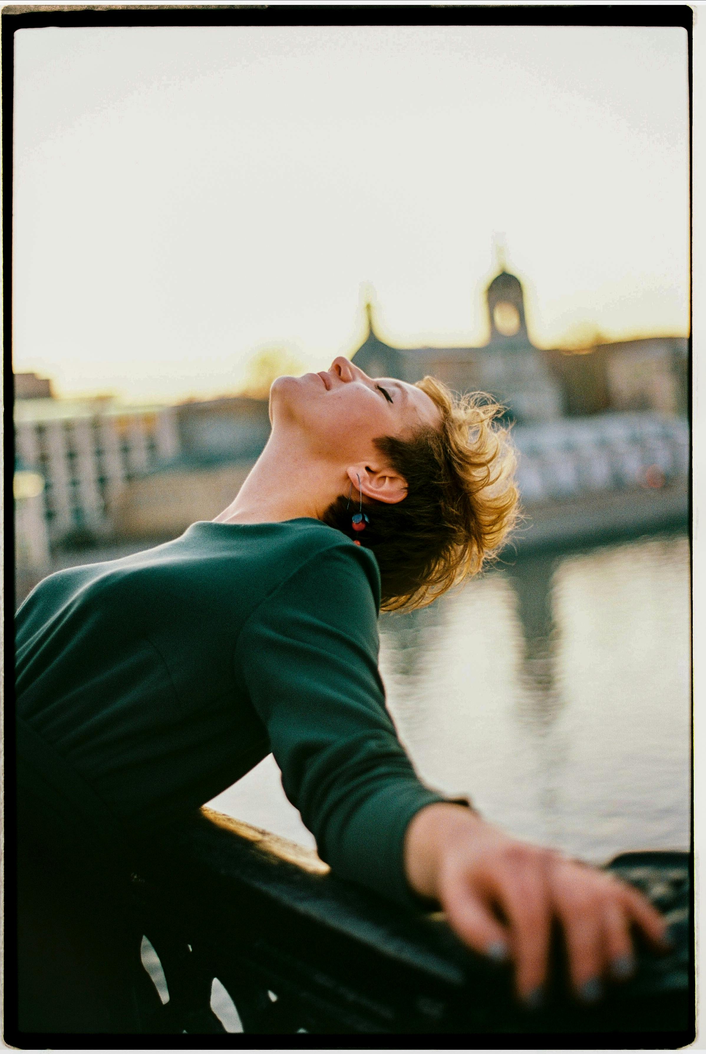 Woman reclining against railing by the river, basking in the sunset glow.