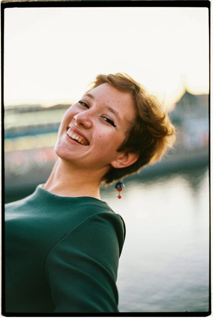 A joyful woman with short hair smiling by the waterfront during sunset.