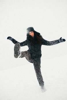 A woman joyfully kicks up snow on a snowy winter day, embracing the cold season.