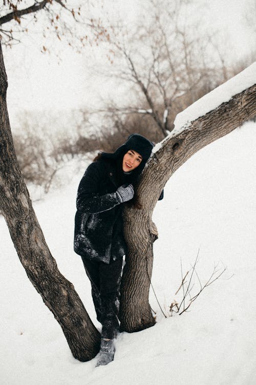 Pretty Girl in Winter Black Furry Jacket and Hat Hugging Tree 