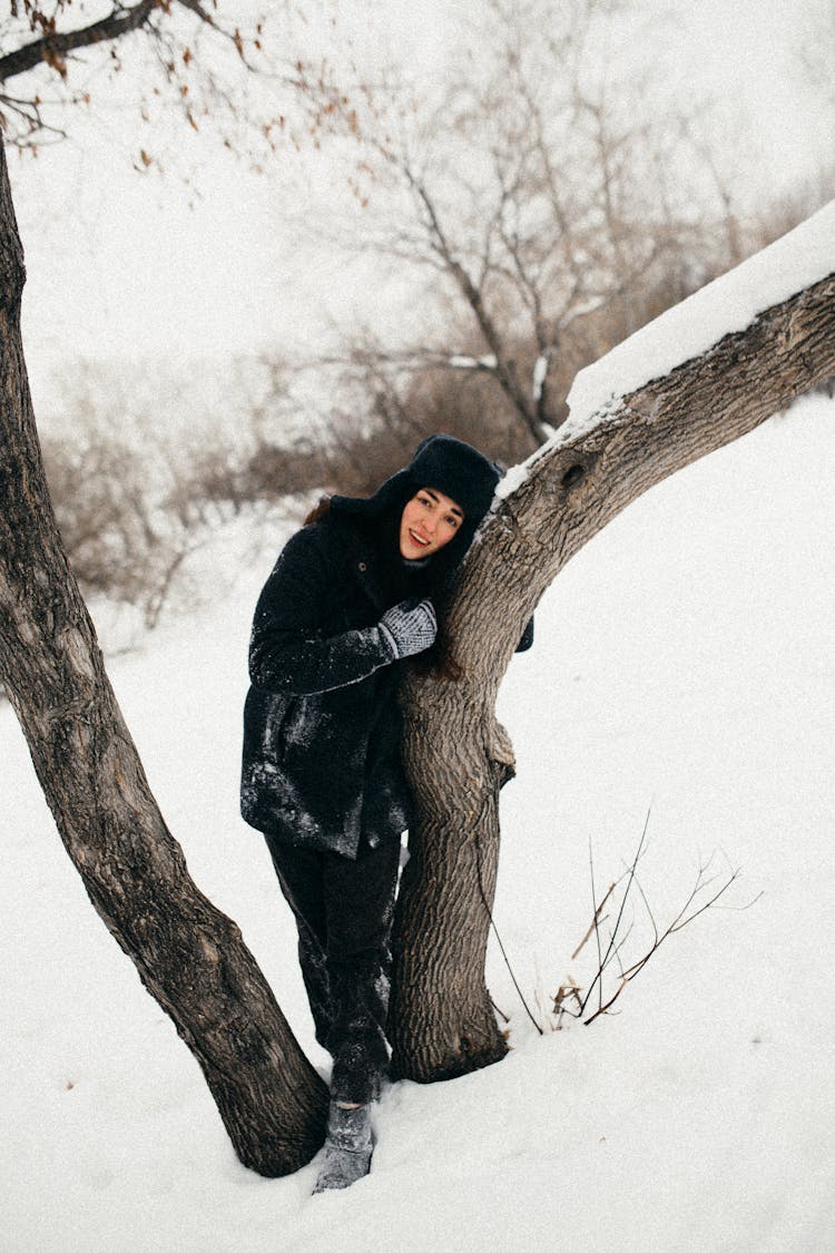 Pretty Girl In Winter Black Furry Jacket And Hat Hugging Tree 