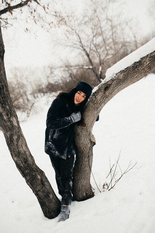 Free A woman in a warm outfit embraces a tree in a snowy landscape. Stock Photo