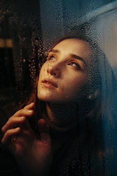 Portrait of a contemplative woman looking through a rain-streaked window, deep in thought.