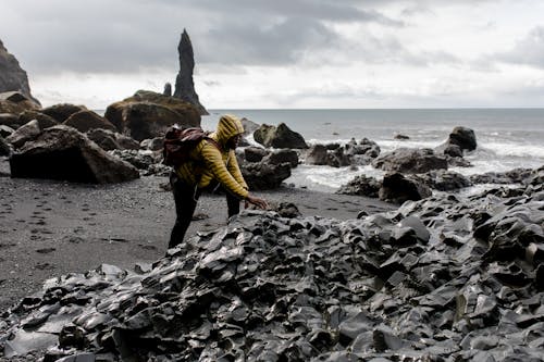 Person Wearing Hoodie Touching Stone in Seashore