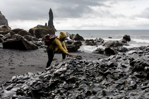 一位旅行者在多云的天空下，探索着冰岛岩石般的黑色沙滩