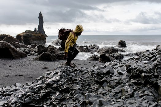 Explorer in yellow jacket navigates rugged volcanic rocks on an Icelandic coast.