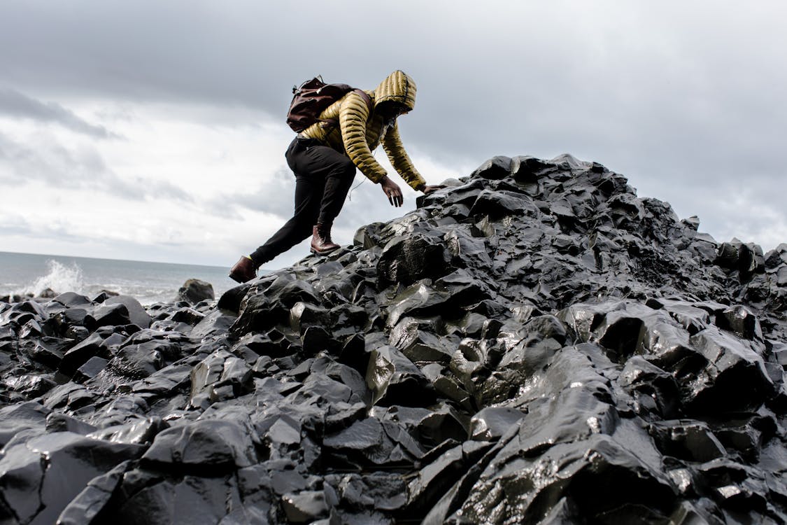 免费 男人穿着连帽衫和黑色裤子爬上一堆岩石 素材图片