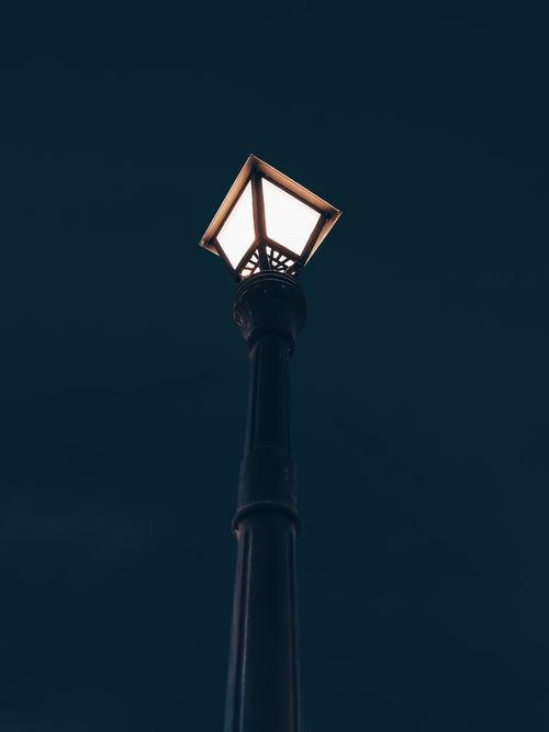 Free A low angle view of a street lamp illuminated against a dark night sky, symbolizing urban solitude. Stock Photo