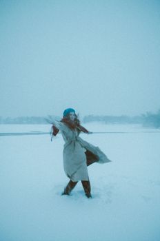 A woman in a coat dances joyfully in a snow-covered field during winter, expressing freedom and joy.