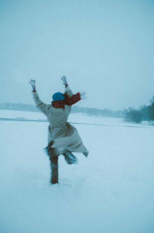 Free A Woman in White Coat Running on a Snow-Covered Field Stock Photo