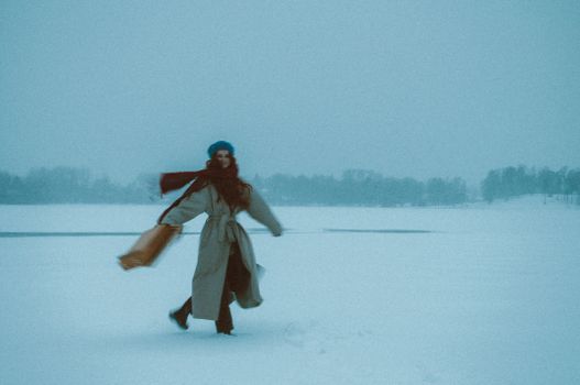 Woman in coat and scarf joyfully walking across a snow-covered field.