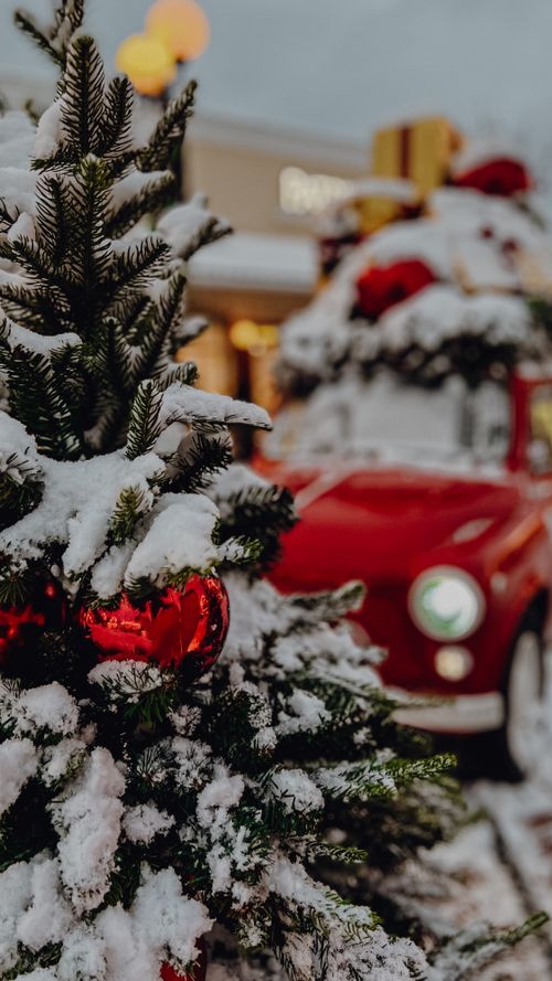 Free A festive winter scene featuring a snowy Christmas tree with baubles and a decorated vintage car in the background. Stock Photo