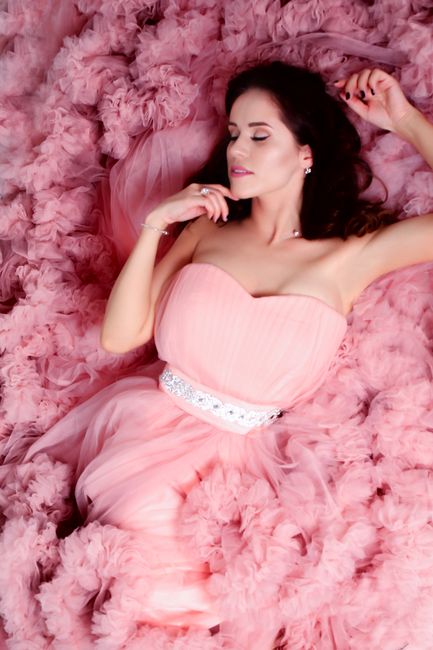 A young woman elegantly posing in a pink strapless dress on pink tulle. Perfect for fashion and beauty themes.