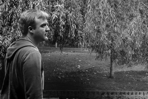 Homme blond de profil près d'un saule pleureur dans un parc