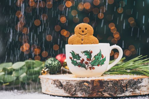 Free Gingerbread man cookie in a holly-decorated cup, surrounded by festive ornaments and snowfall. Stock Photo