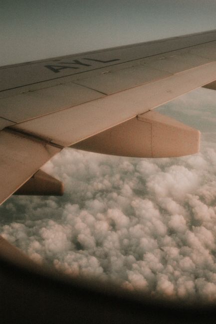 View of an airplane wing with a sea of clouds below during sunset, captured from a window seat.
