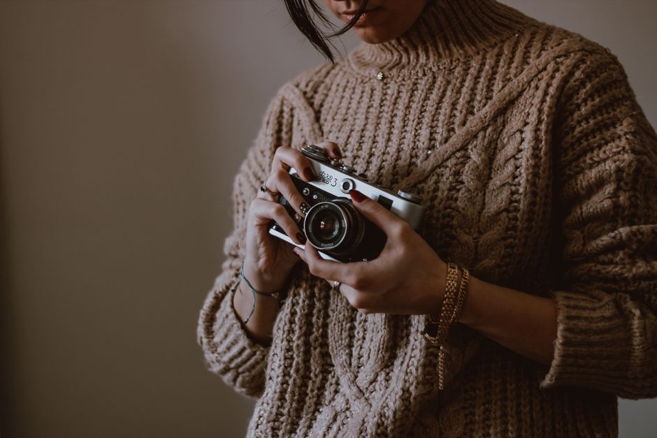A stylish woman in a knitted sweater holds a vintage camera, creating a warm and artistic vibe.