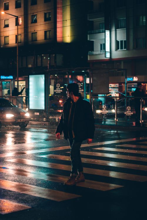 Free A man crossing a city street at night in Konya, Turkey, with vibrant lights in the background. Stock Photo