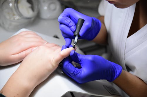 Person in Blue Gloves Applying Nail Polish on Fingernail